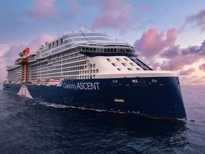 A prominent blue cruise ship, Celebrity Ascent, navigating the ocean waves with a bright sky above.