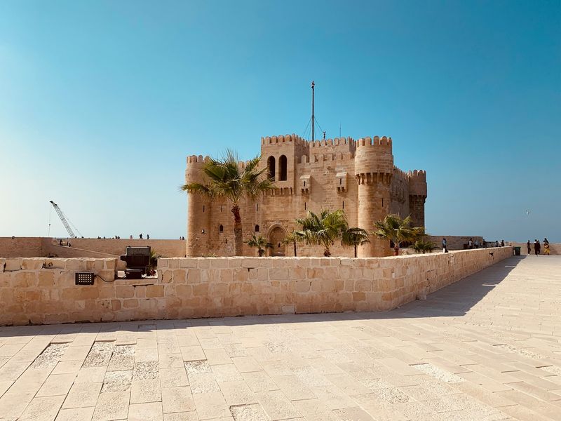 A castle in Alexandria stands prominently beside a road, showcasing its historic architecture against a clear sky.