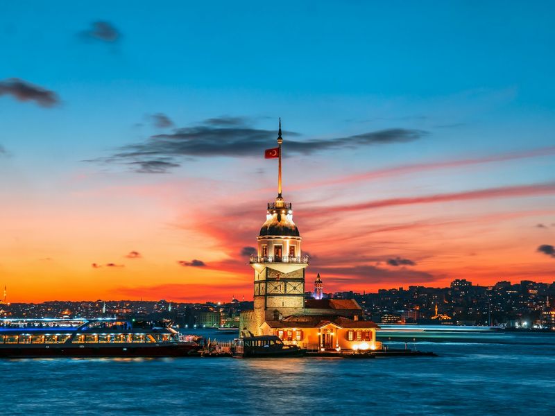 Sunset over the blue sea with a tall tower silhouetted against the vibrant sky in Istanbul.