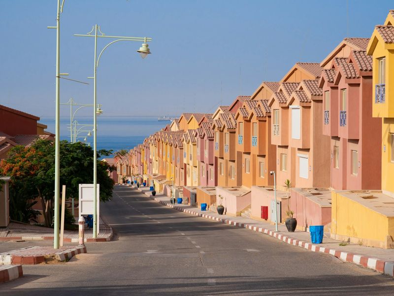 A row of colorful houses lined up along a coastal street in Ain Sokhna, with clear blue skies above.